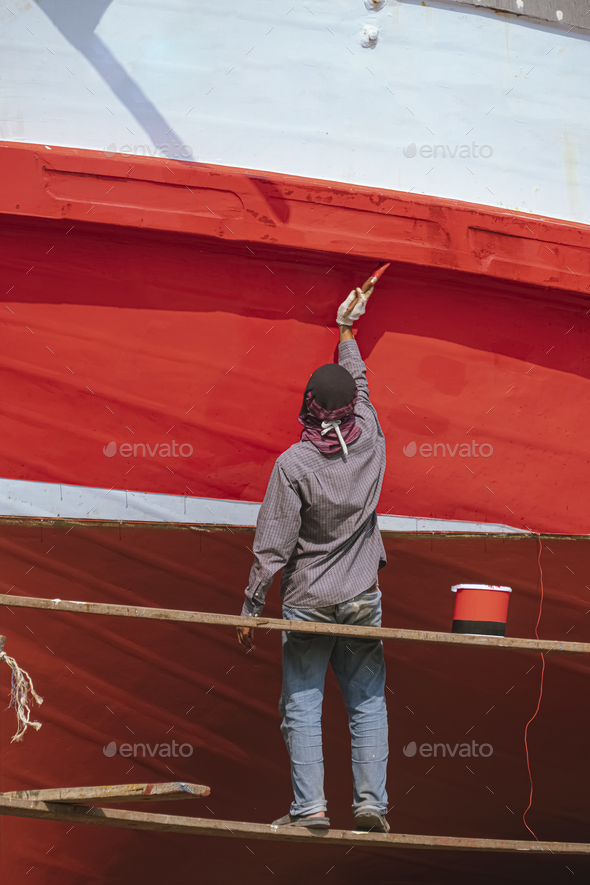 Asian painter on hanging platform is repainting hull of the old wooden